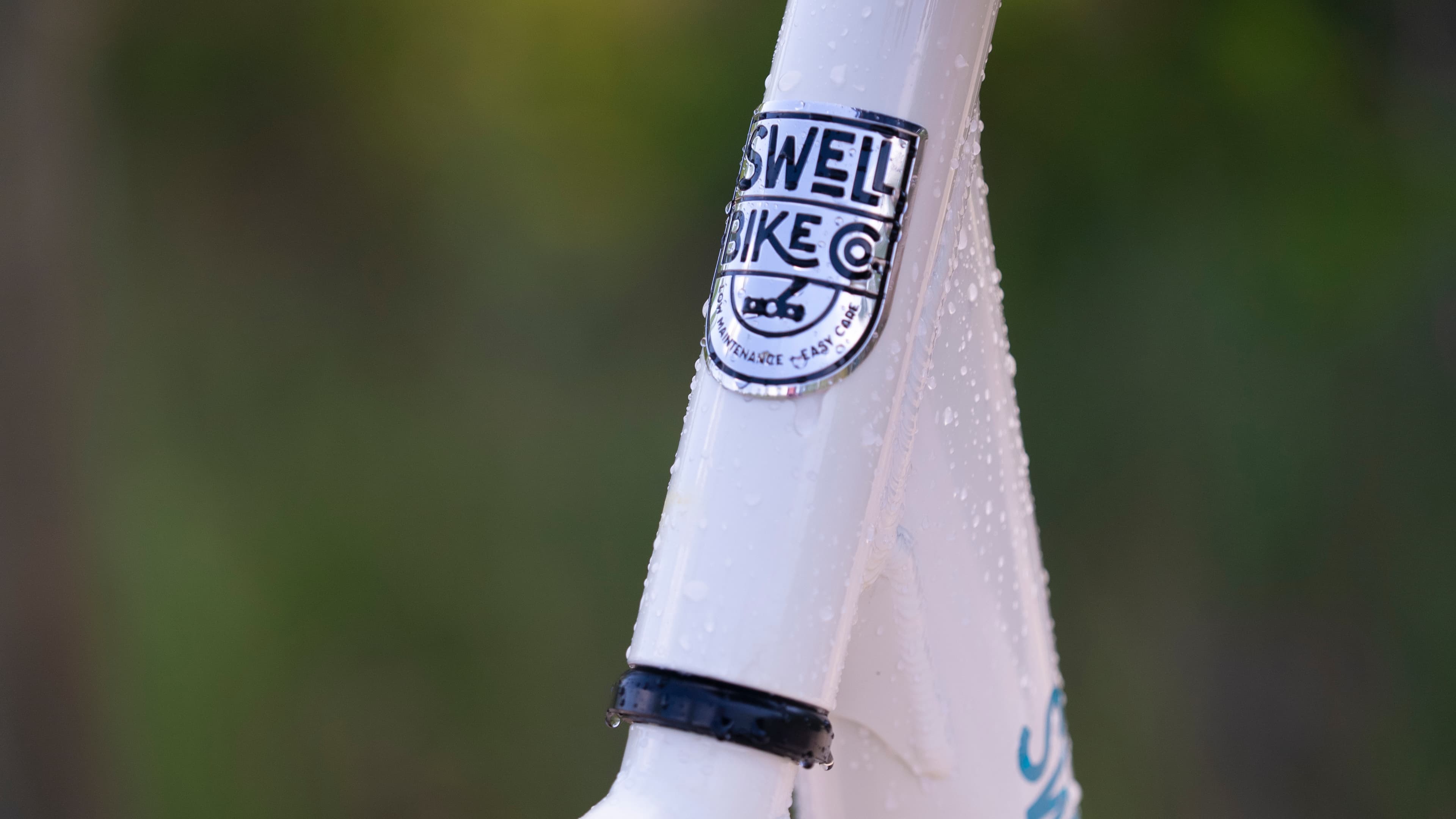 The Swell Bike Co. head badge on a white frame, beaded with water