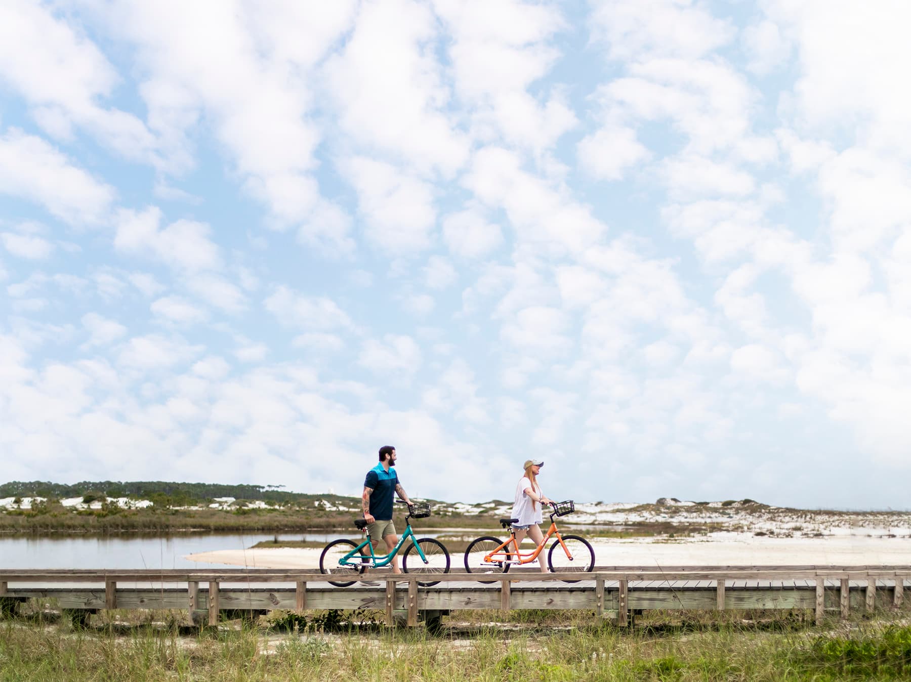 Two riders on Swell bikes crossing a boardwalk through the dunes