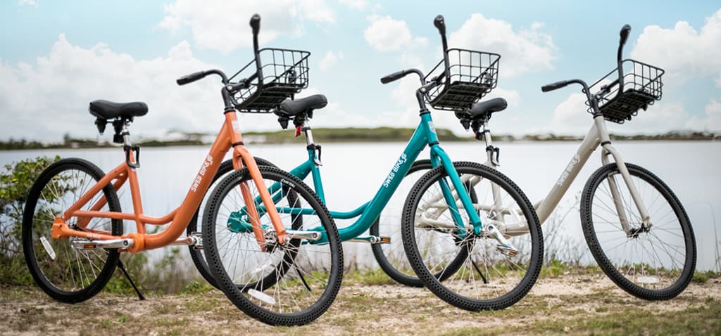 Three Swell bikes in orange, teal and cream lined up by the water
